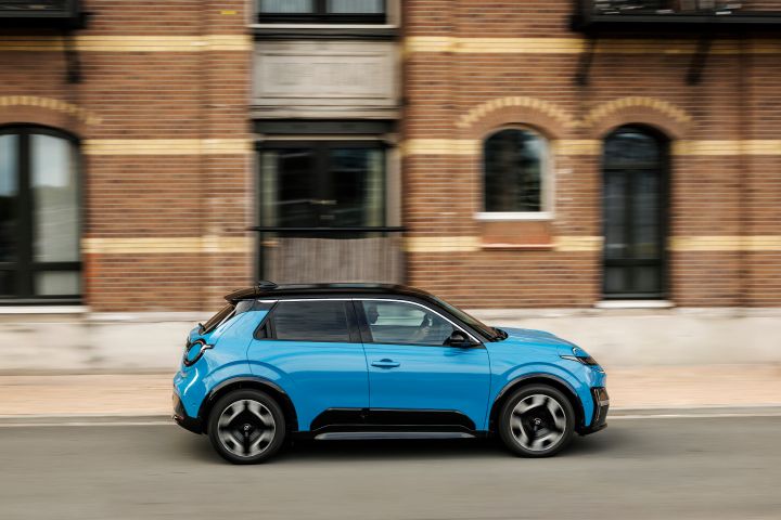 Seitliche Fahraufnahme eines blauen Nissan Micra vor einem braunen Backsteingebäude
