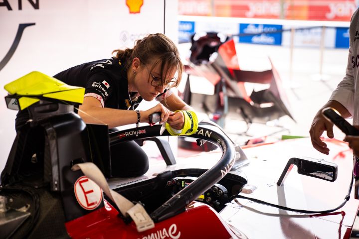 A woman in Nissan Formula E gear on a laptop near the race track.