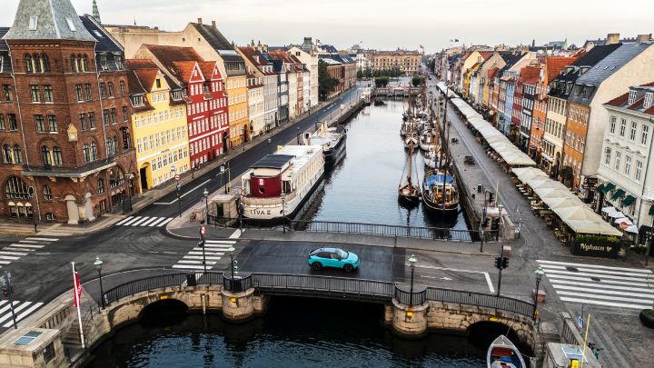 Luftaufnahme der bunten Altstadthäuser in Kopenhagen zu beiden Seiten eines Kanals, zentral auf einer Brücke in der Bildmitte fährt ein türkiser Nissan LEAF