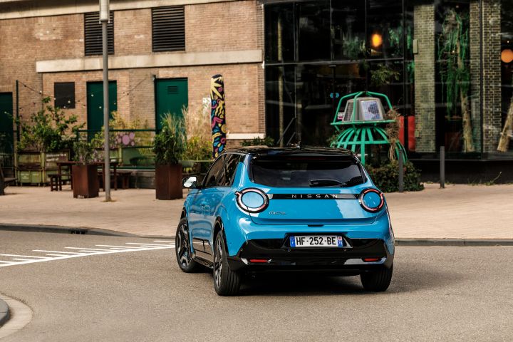 Blick auf das Heck eines blauen Nissan Micra, der zwischen zwei Gebäuden nach links abbiegt