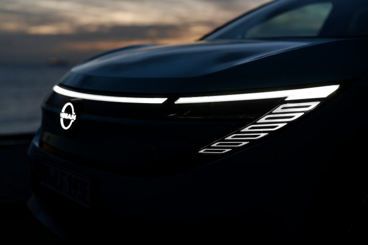 Seitliche Detailaufnahme der Frontpartie des neuen Nissan LEAF bei Dunkelheit, man sieht die eingeschalteten Scheinwerfer und das leuchtende Nissan Logo