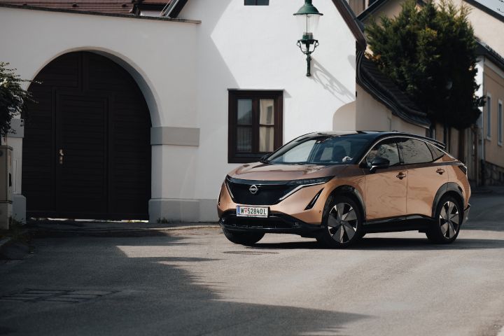 Ein kupferfarbener Nissan Ariya parkte vor einem weißen Gebäude