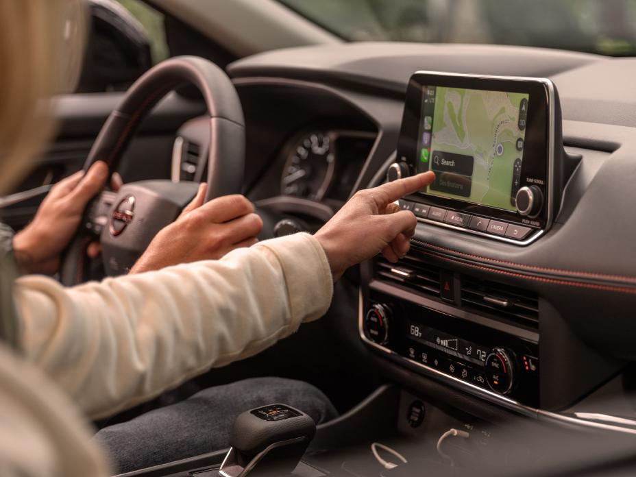 The steering wheel and infotainment screen is used by two individuals inside the 2025 Nissan Rogue rock creek.
