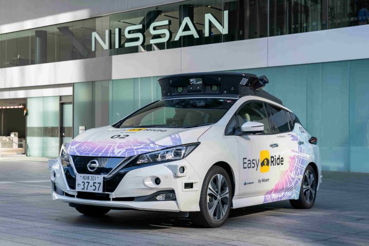 A white Nissan LEAF with autonomous mobility equipment installed on its roof parking in front of Nissan office