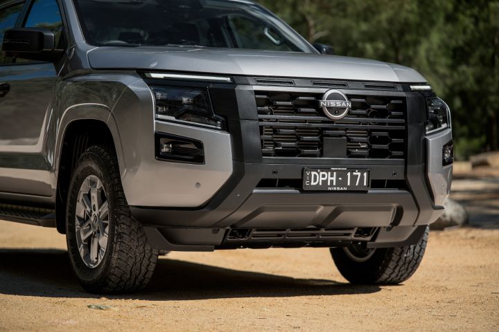 2026 Nissan Navara ST dual cab ute finished in Summit Silver shown in a low front-end close-up with black grille detailing, bumper design and front wheel.