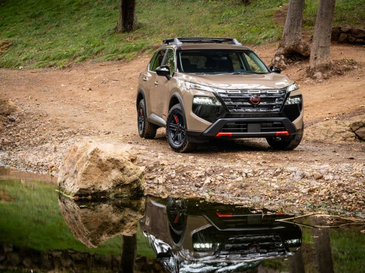 Vue ¾ avant droite du 2026 Nissan Rogue rock creek Garé au bord d’un ruisseau reflétant son image.