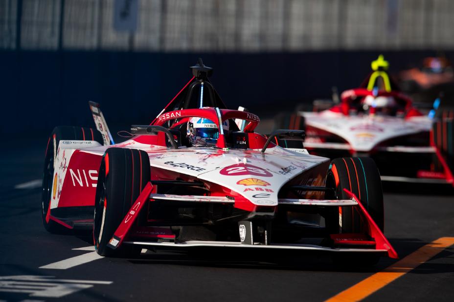 Nissan Formula E raceauto op een circuit met andere auto’s erachter en donkere achtergrond