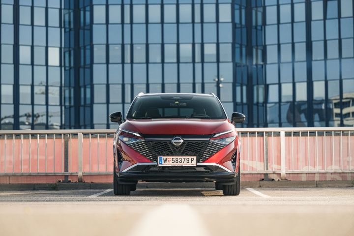 Frontansicht Nissan Qashqai in Fuji Sunset Red vor einem verglasten Hochhaus