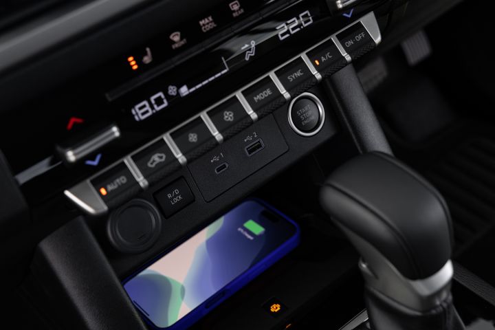 Detailed view of the lower centre console in a 2026 Nissan Navara ST-X, showing dual-zone climate controls, a wireless charging tray with a phone, USB-C and USB-A ports, a rear differential lock switch, and the gear selector.
