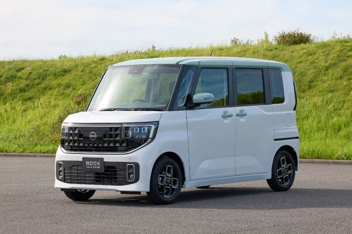The new Nissan Roox kei car, finished in a White Pearl and Celadon Green two-tone color scheme, is parked on the road. The bright body colors blend with the surroundings, creating a refined and stylish impression.