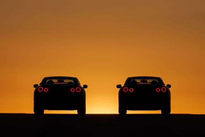 Silhouette of two special edition Nissan GT‑R rear ends with a dark foreground and sunset in background