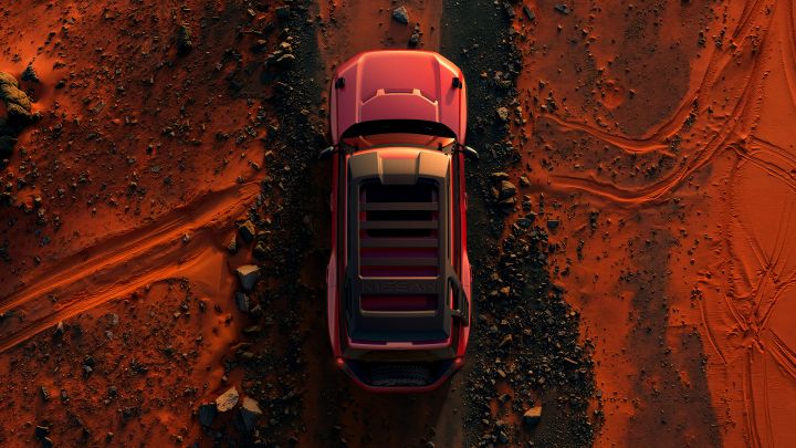 A top-down view of a red Terrano PHEV Concept driving forward (toward the top of the frame) across a desert landscape. The vehicle is centered, surrounded by reddish sand, tire tracks, and scattered rocks.