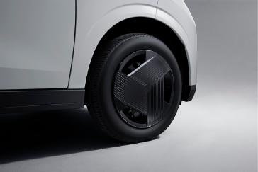 白い「日産サクラ」の前輪部分を接写した画像。黒いホイールデザインがはっきりと見え、背景は落ち着いたグレーで統一されている。