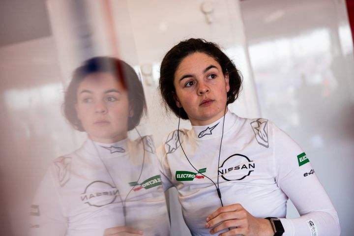 Porträtfoto von Abbi Pulling in ihrem weißen, feuerfesten Rennanzug in der Nissan Teamgarage beim Rookie Test in Madrid