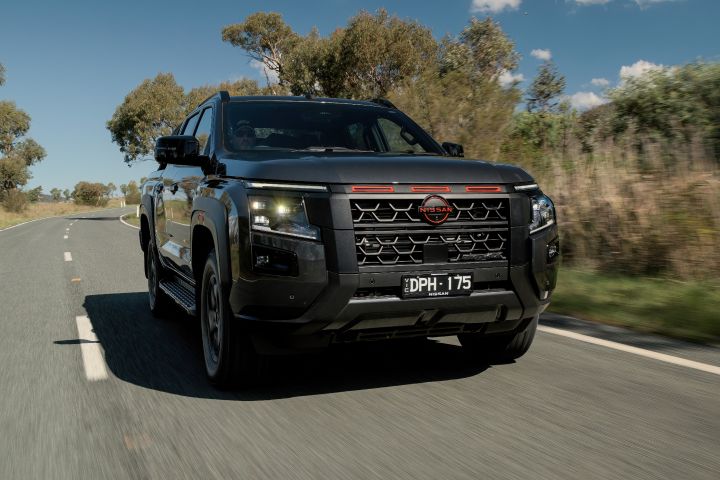 2026 Nissan Navara PRO-4X finished in Boulder Grey shown in a closer rolling front-left view with patterned grille, number plate and chunky tyre sidewalls.