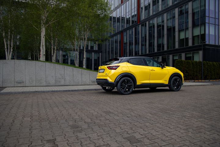 Żółty Nissan Juke stojący bokiem na tle budynku i drzew