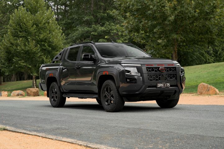2026 Nissan Navara PRO-4X finished in Boulder Grey shown from the front three-quarter angle with red-accented grille, black bumper and flares, matt black wheels and all-terrain tyres.