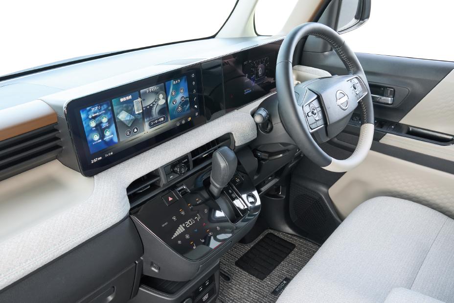 The driver's seat of the new Nissan Roox kei car, featuring a steering wheel, digital display, gear shift lever, and other control devices. The interior has a modern and sophisticated design.
