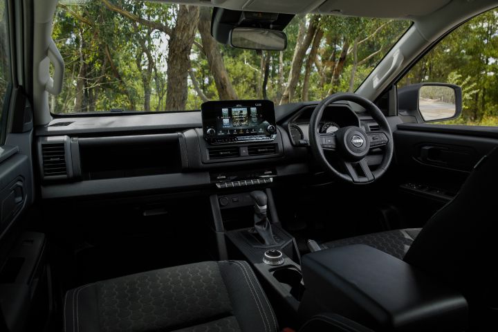2026 Nissan Navara SL dual cab ute finished in Alpine White with a wide interior view across the front seats, dashboard, infotainment screen, console storage and manual-style cabin layout.