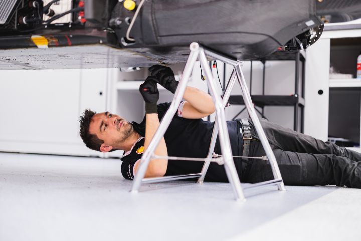 Unter einem aufgebockten Nissan Formel E Rennwagen liegt ein schraubender Mechaniker
