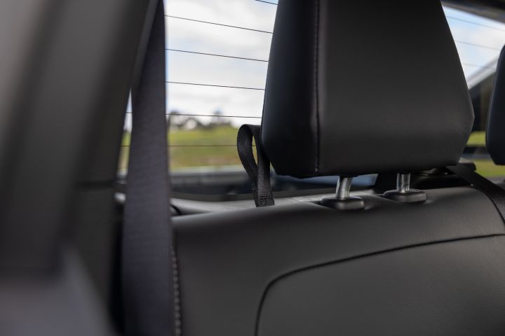 Close-up from the rear cabin of a 2026 Nissan Navara ST‑X showing a rear headrest, seatbelt webbing, and the rear window area with the exterior tray and landscape softly out of focus.
