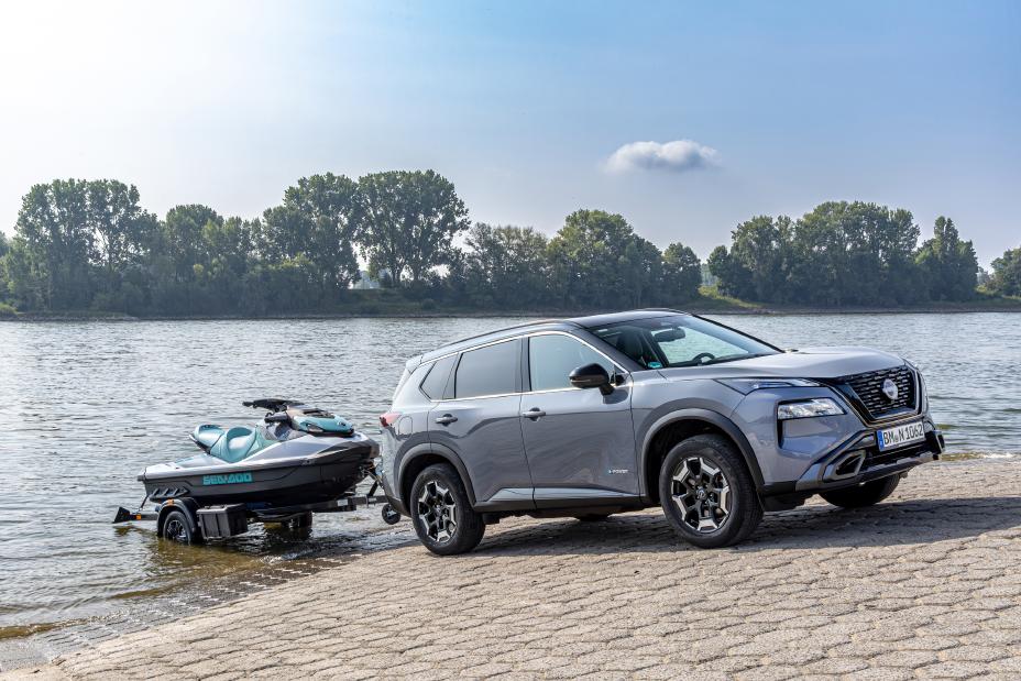 Ein metallicgrau lackierter Nissan X‑Trail N-Trek mit Bootsanhänger steht bei Sonnenschein schräg an einer gepflasterten Rampe am Fluss Rhein, der Bootsanhänger mit Jetski steht im Wasser