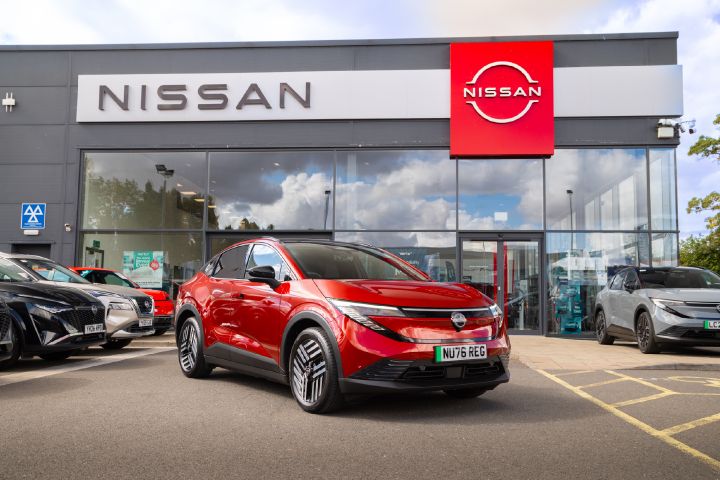 Front three-quarter view of a red Nissan LEAF outside a Nissan dealership