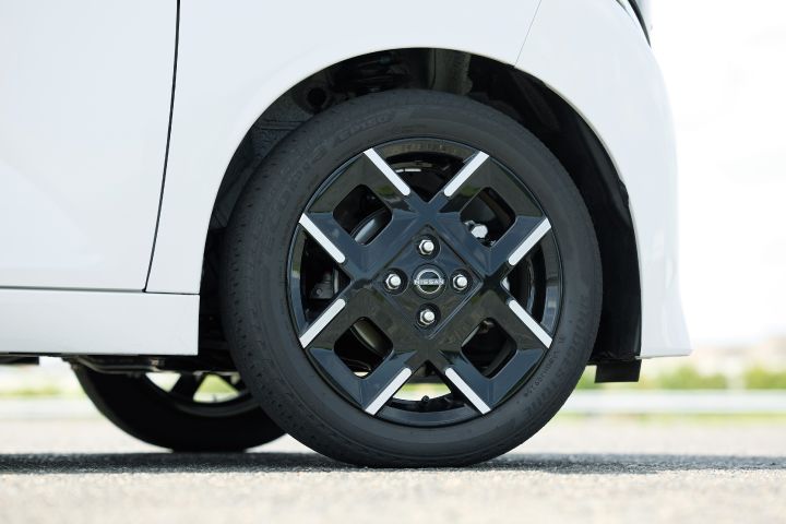 Close-up photo of the black wheel and tire on the white body of the new Nissan Roox kei car. The wheel features silver accents and a distinctive design. A portion of the car's body is also visible.