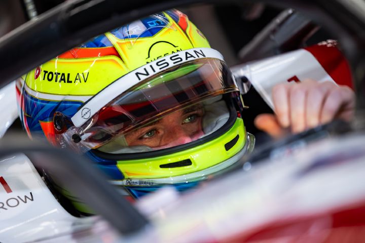 Nahaufnahme von Oliver Rowland, der mit einem leuchtend gelben Rennhelm im Cockpit seines Formel-E-Wagens sitzt und nach vorne blickt. Um den Fahrer herum sind Teile des weiß-roten Fahrzeugs zu sehen, während der Hintergrund unscharf ist.