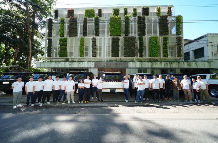 Group of people in white shirts standing in front of SUVs and a building with a vertical garden facade