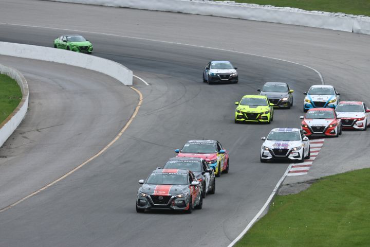 Several Nissan Sentra race cars driving around the bend of a race track with grass in the background