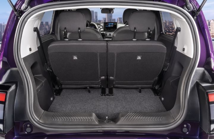 Fotografia que mostra a área de carga traseira de um automóvel compacto roxo, destacando o espaço de arrumação e o design interior. Bancos traseiros rebatíveis separadamente, piso alcatifado, painéis laterais, painel de instrumentos e o horizonte da cidade visível através do habitáculo.
