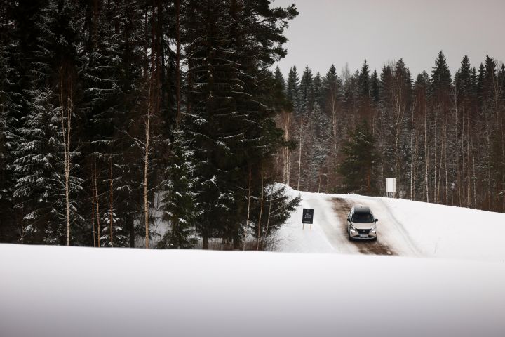 Im Hintergrund fährt ein silberner Nissan X‑Trail e‑Power e‑4ORCE einen steilen Hügel in verschneiter Landschaft herab