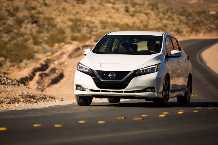 A white Nissan LEAF driving down a road