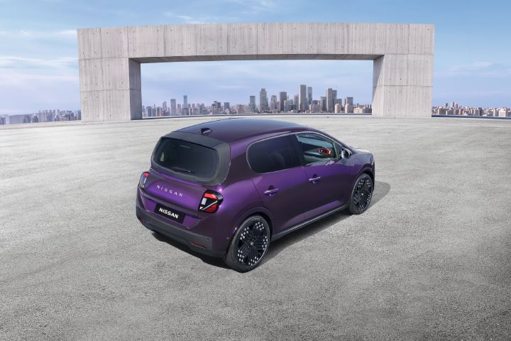 Bakre trekvart av en lilla Nissan PIXO elektrisk bybil parkert i et moderne urbant miljø, med en bysilhuett i bakgrunnen