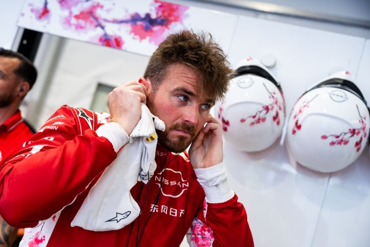 Oliver Rowland bereitet sich in der Nissan Formel E Box auf eine Trainingseinheit vor: Er trägt seinen roten Rennanzug und setzt gerade seine Kopfhörer ein.