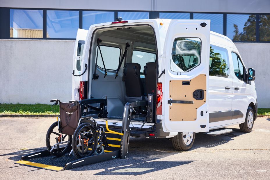 3/4 Heckansicht eines weißen Nissan Interstar-e mit MobiTEC Ausbau, an dessen Heck der Rollstuhllift auf Straßenniveau heruntergelassen wurde, ein Rollstuhl steht auf dem Lift