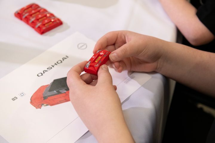 A school child holding a LEGO piece infront of LEGO instruction sheets.