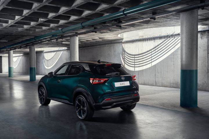 Rear three-quarter view of the Nissan JUKE Pulse driving through an underground industrial space, showcasing its distinctive rear lights, compact crossover stance, and contrasting black roof.