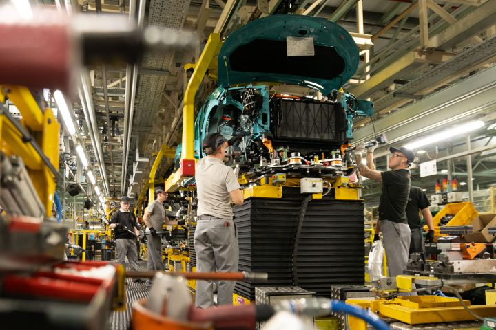 Nissan LEAF auf der Fahrgestelllinie im Nissan-Werk in Sunderland, mehrere Menschen arbeiten an dem Fahrzeug