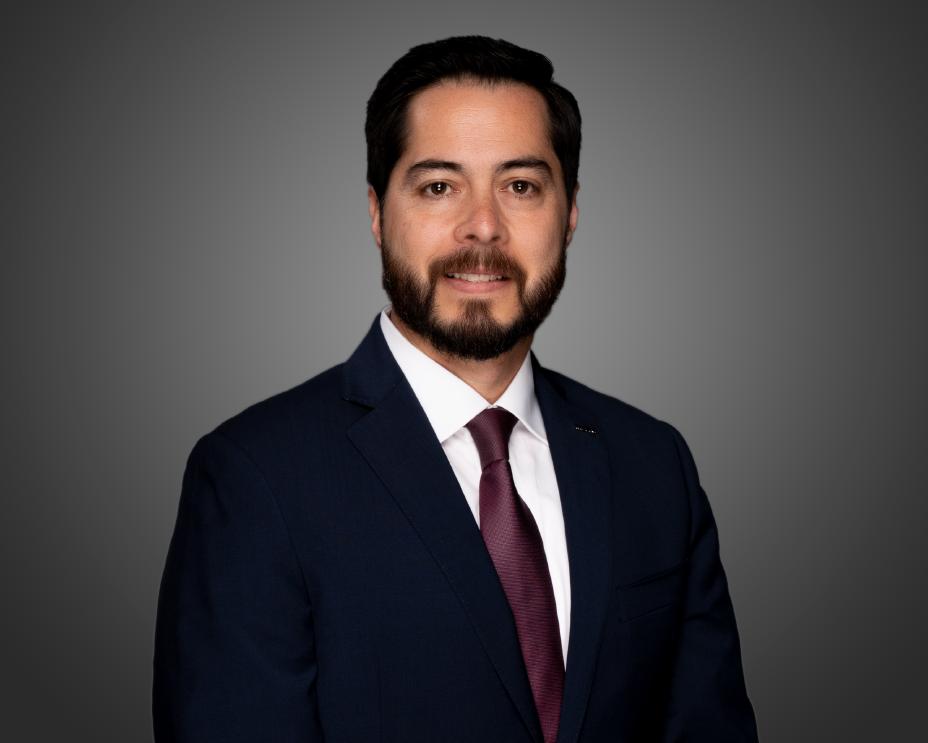 Leo smiling in a blue suit and red tie form the mid arms up.