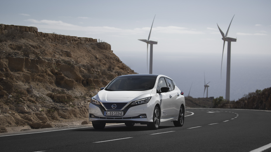A Nissan LEAF driving down a road away from wind turbines