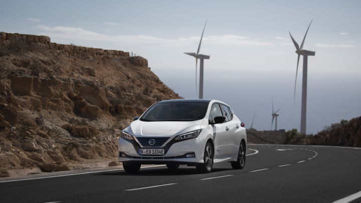 A Nissan LEAF driving down a road away from wind turbines