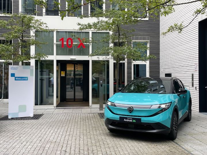 Ein türkisblauer Nissan LEAF steht vor der grauen Steinfassade des Google Gebäudes in München, links neben dem Auto steht ein Schild mit der Aufschrift Welcome