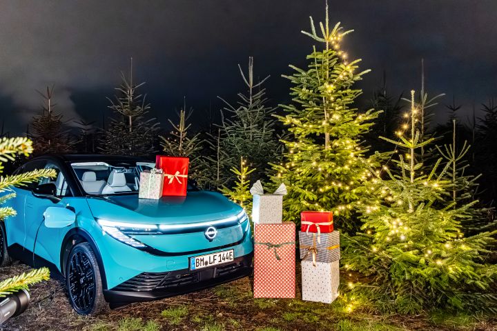 Ein türkisblauer Nissan LEAF steht zwischen Weihnachtsbäumen, auf der Fronthaube und neben dem Auto stehen mehrere Weihnachtsgeschenke