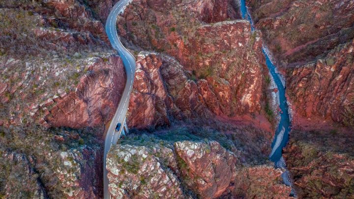 Vue aérienne d'une route sinueuse qui serpente à travers un canyon rocheux et rouge, sur laquelle se trouve la Nissan Ariya NISMO