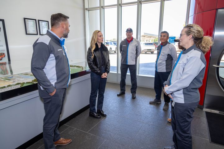 Brie Larson stands with four other people in a lobby with floor to ceiling windows.