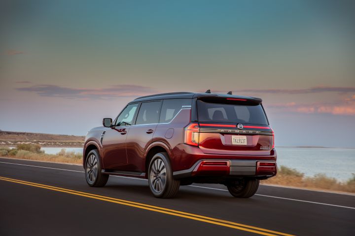 Left rear 3/4 view of a 2025 Nissan Armada driving on a road at dusk with a body of water beside it.