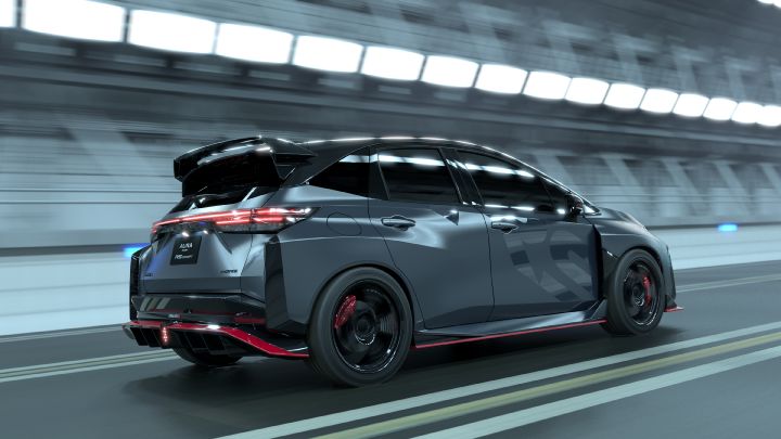 A silver and black two-tone sports car, the Aura Nismo RS Concept, speeding through a tunnel in a rear-left angled view. The vehicle features a large rear wing, with a black plate displaying white text reading 'AURA NISMO RS CONCEPT' at the center of the rear, and a red accent line along the lower bumper. The black wheels with red brake calipers stand out, while the blurred tunnel walls in the background emphasize motion and dynamic speed