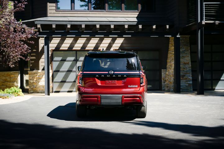 Rear view of a red 2025 Nissan Armada parked in the driveway of a brick house.